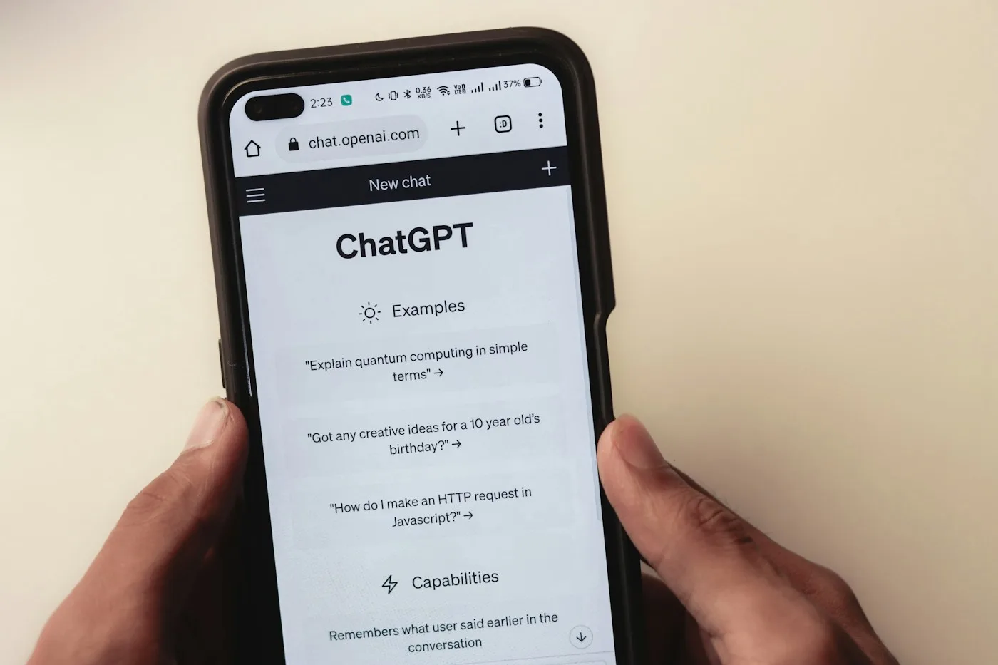 Hands holding a smartphone showing the ChatGPT start screen with example prompts